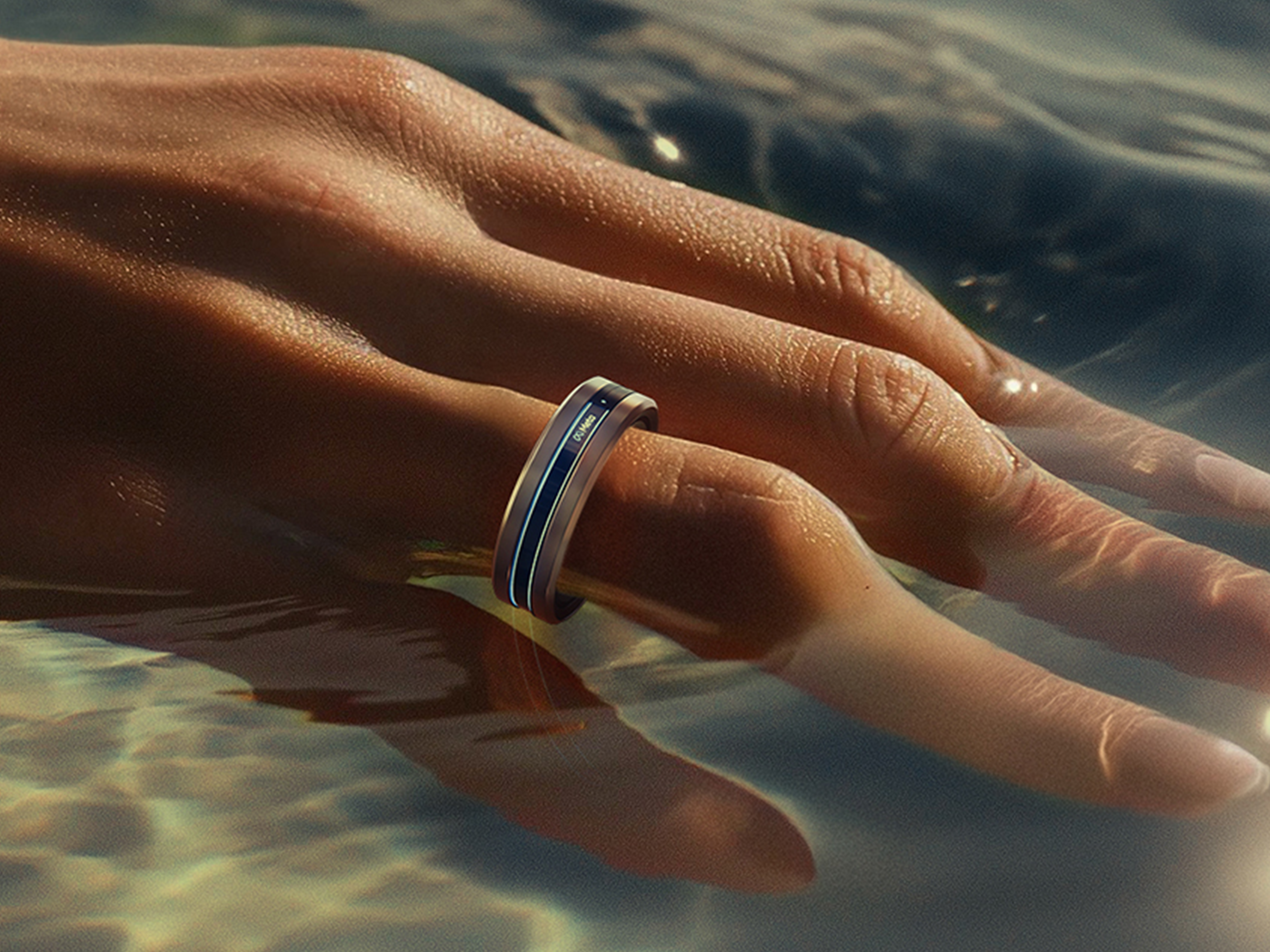 Hand wearing Meta Ring, ring finger dipped in sunlit water with blue accent band visible