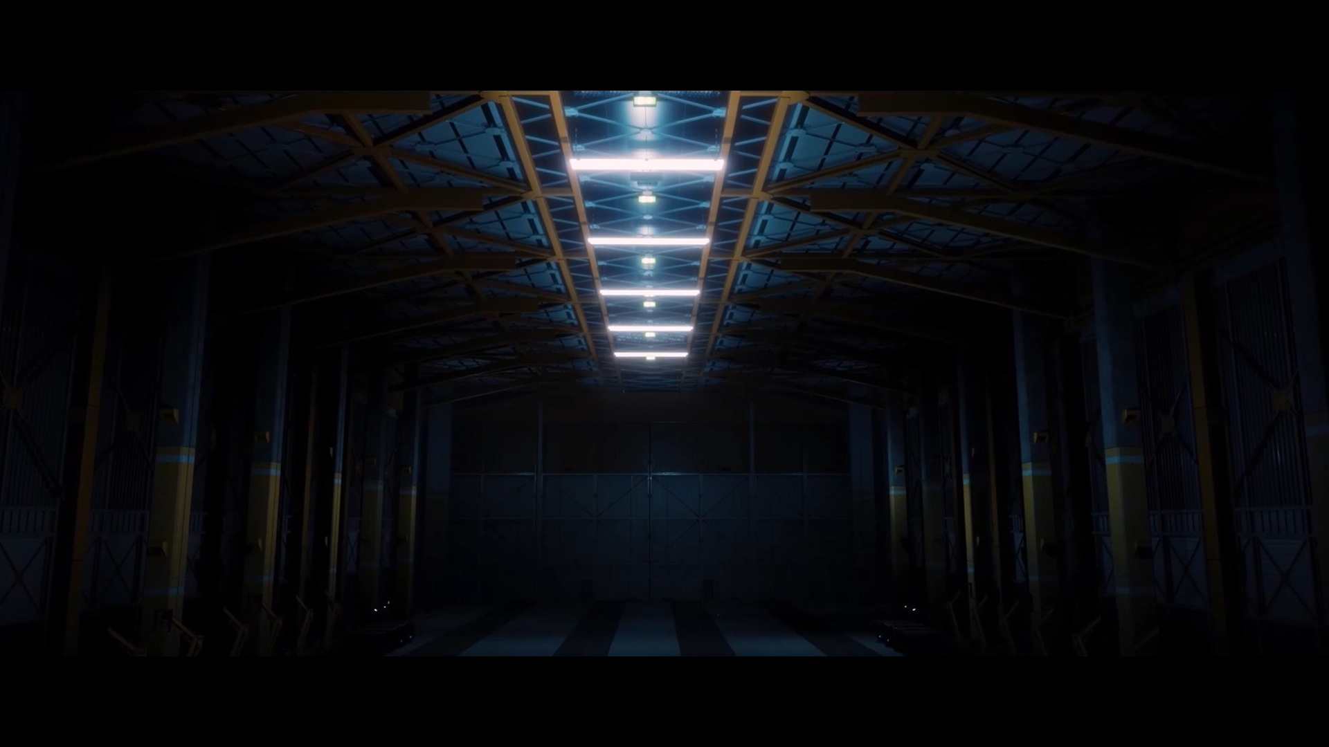 Symmetrical industrial hangar with a row of overhead fluorescents leading to a closed bay door